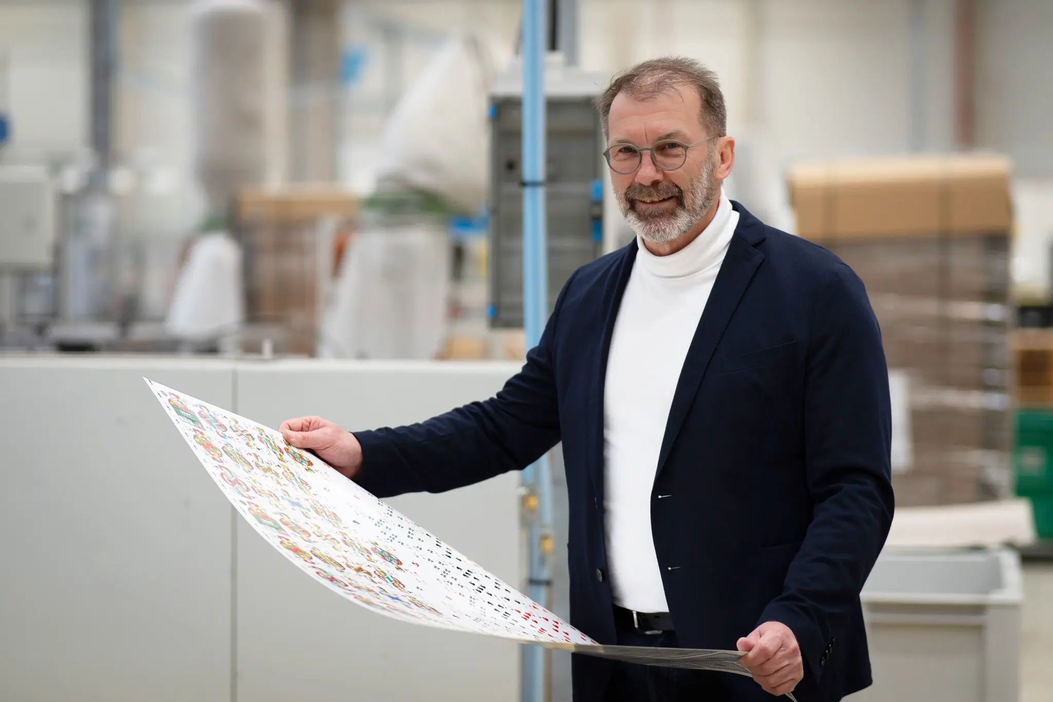 Geschäftsführer Jürgen Gehr in Fabrik mit Druckbogen in der Hand in die Kamera lächelnd